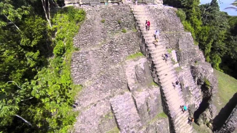 photo of persons climbing to the top of a temple at lamanai mayan ruins in belize